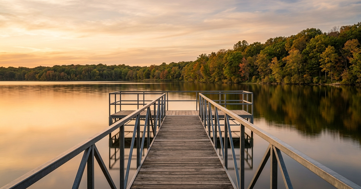 Wooden dock extending into calm lake at sunrise with autumn trees reflected in water, seasonal pier removal Southwest...
