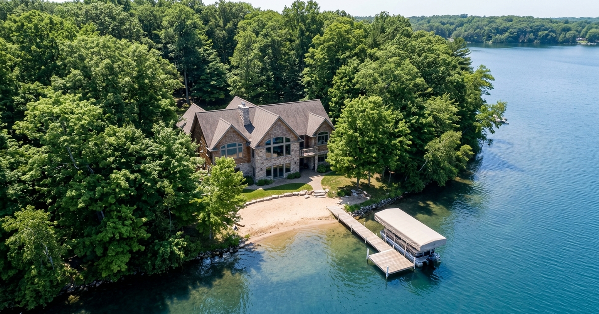 Luxury lakefront estate on Southwest Michigan lake with stone exterior, private beach, and boat dock surrounded by trees