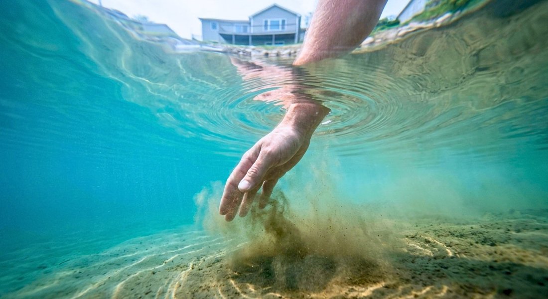 Hand creates ripples above the lake bottom during a water test.